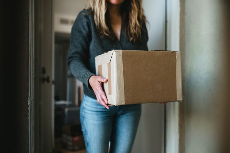 Blonde woman standing at apartment door holding a box that arrived