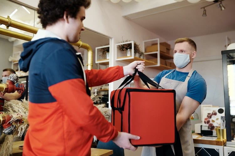 A food delivery driver taking a thermal bag from a restaurant worker