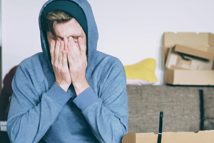 Male in blue hoodie covering his face with hands in stressed moment