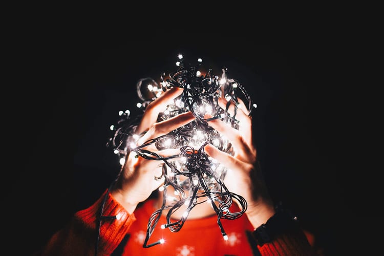 Hands holding up a cluster of white Christmas lights in front of face in the dark