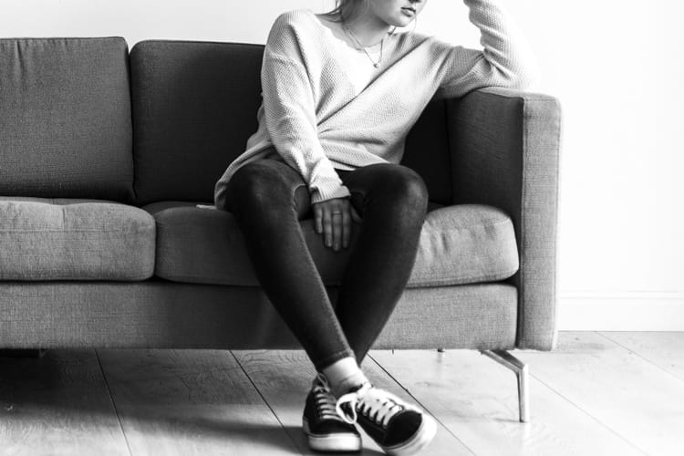 Black and white photo of a woman sitting on a couch with worried or thinking posture