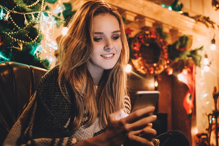 Woman smiling at phone sitting in Christmas decorated living room