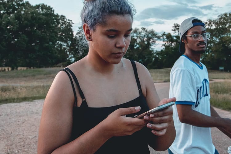 Woman with dyed silver hair in a bun looking at phone in the park