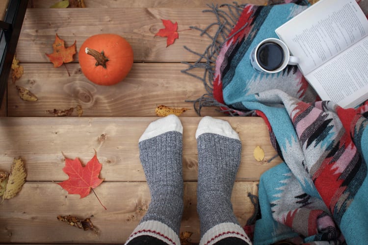 Pair of feet in cozy grey socks with fall decor around including pumpkin and coffee