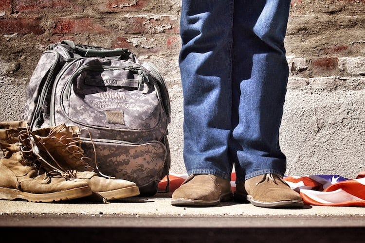 A man in jeans standing next to a camouflage backpack and military boots