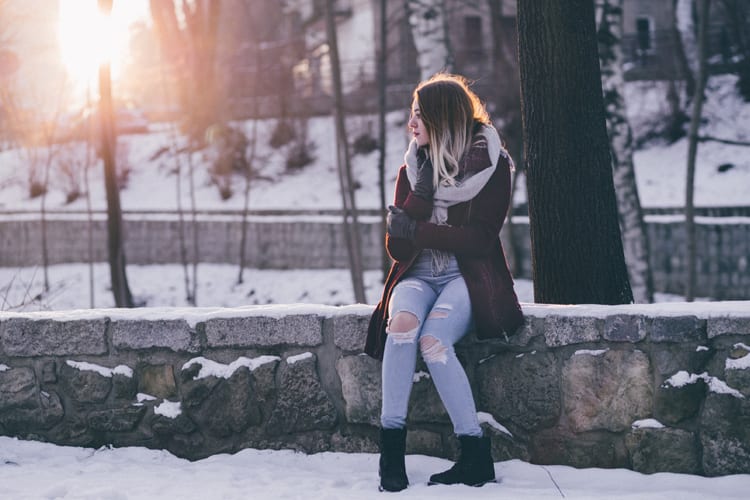 Woman sitting on a low wall in the park with snow all around