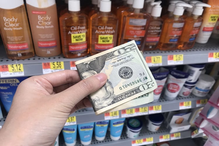 Hand holding a twenty dollar bill in front of a Walmart beauty aisle shelf