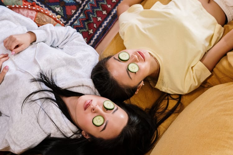 2 asian females lying on the couch with cucumbers over their eyes for at-home spa