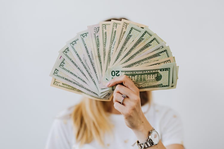 Blonde woman holding money spread out like a fan in front of face