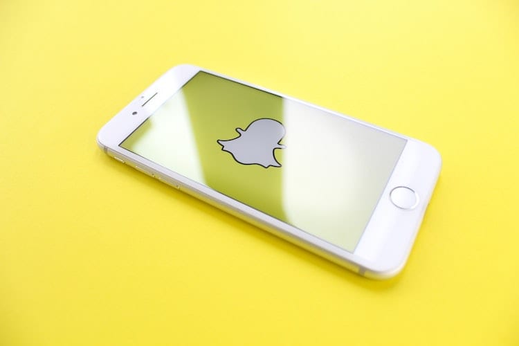 A white iPhone open to the Snapchat logo against a yellow background