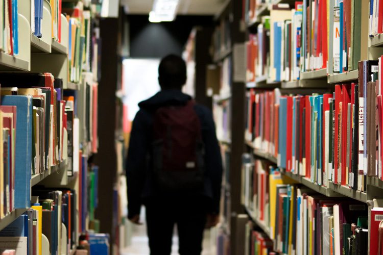 student with backpack standing in between library shelves